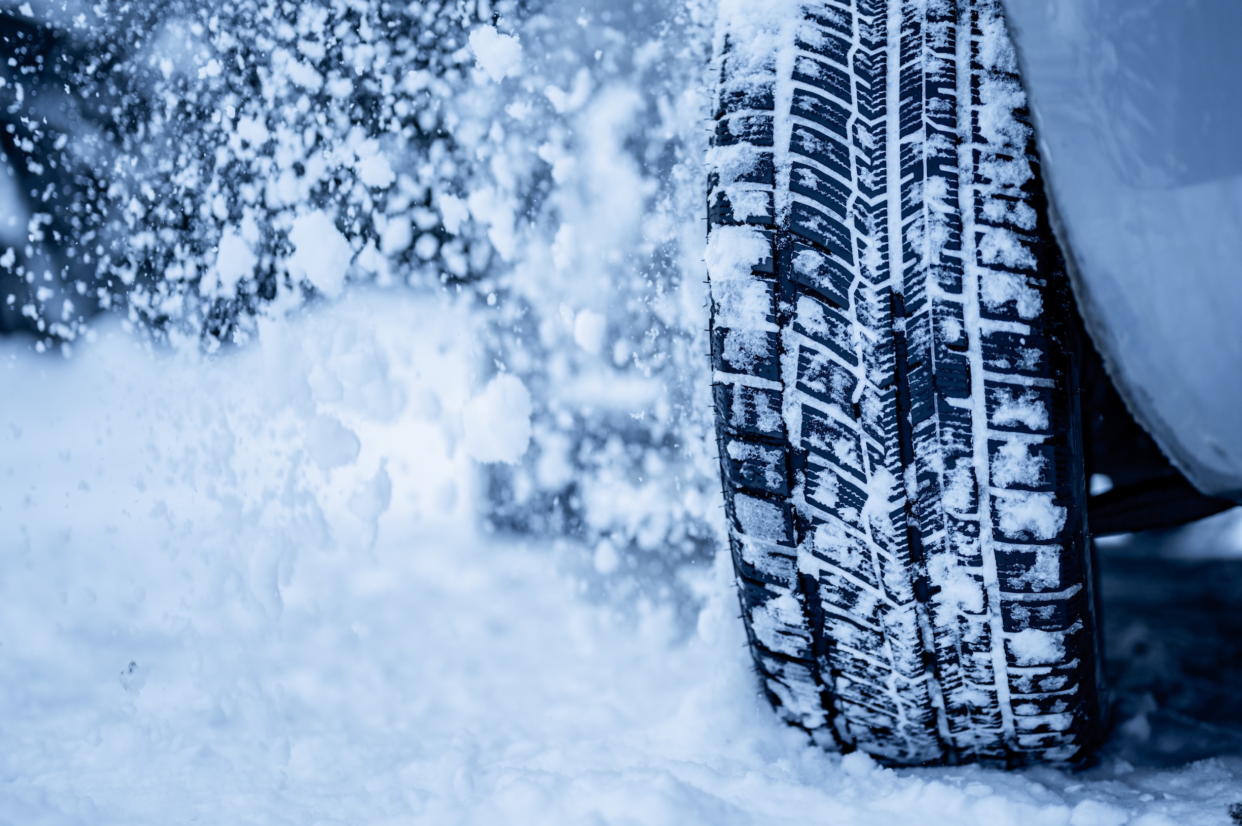 close up of car tire cutting through snow, flinging snow into the air as it drives through.