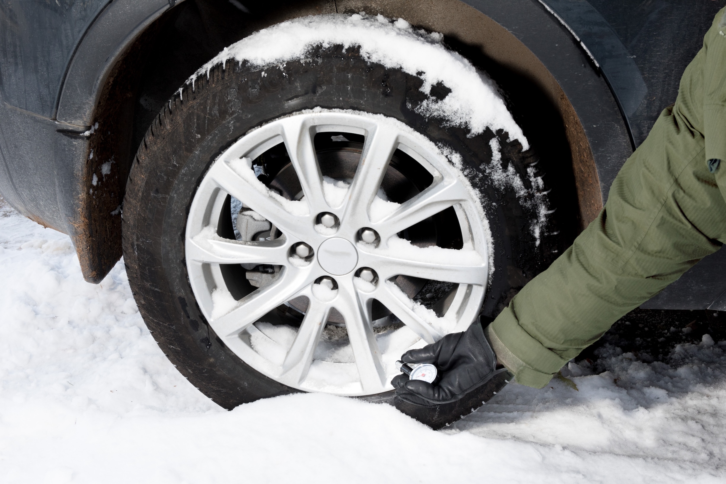 Person checking the tire pressure on a snowy, winer day.