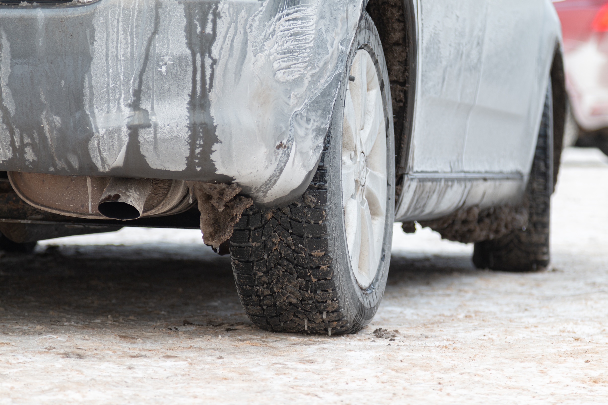 Car with snow and salt on the tires and vehicle body sitting on a snowy road